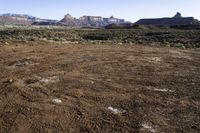 a barren field and mountain ranges, with a few snow patches in the dirt on the ground