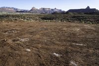 a barren field and mountain ranges, with a few snow patches in the dirt on the ground