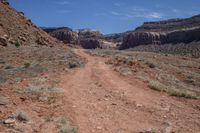 a dirt road winding up in a vast wilderness area with a large cliff wall and deep canyons in the distance