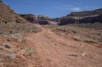 a dirt road winding up in a vast wilderness area with a large cliff wall and deep canyons in the distance