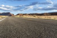 an empty road runs through a vast desert area with rocky hills in the background and blue skies