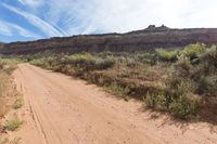 a person is riding down a dirt road in the desert with a sky background and trees