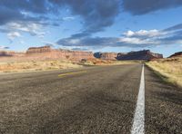 a lonely asphalt road under a blue sky with some clouds in the distance and some mountains on both sides