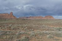 a dirt path leading to some large rock formations, as if in the distance is a green grass field and shrubs