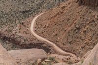 a vehicle traveling down a winding rocky road with sparse vegetation on either side of it