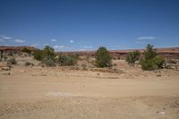 a dirt road in the middle of a barren area and red mountains with sparse vegetation