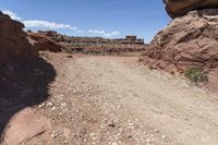 a dirt and gravel road winding through the mountains on a sunny day at arches in the background