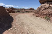 a dirt and gravel road winding through the mountains on a sunny day at arches in the background