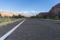 a lonely, long paved road in the desert landscape with mountains in the background and a few trees