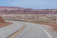 the winding road is covered by rocky cliffs and desert like terrain as a lone motorcycle passes through it