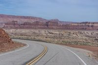 the winding road is covered by rocky cliffs and desert like terrain as a lone motorcycle passes through it