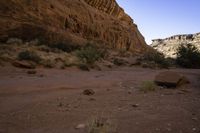 a large rock in a narrow section of sand in the mountains near a river and rocks