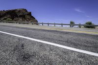 an empty road by a mountain in the desert with a bridge over it and mountains in the background