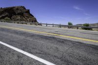 an empty road by a mountain in the desert with a bridge over it and mountains in the background