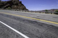 an empty road by a mountain in the desert with a bridge over it and mountains in the background