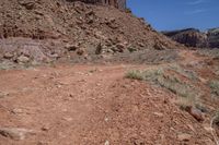 dirt road with rocky terrain at bottom and mountains on either side, blue sky in the background