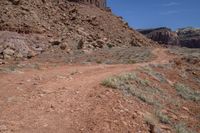 dirt road with rocky terrain at bottom and mountains on either side, blue sky in the background