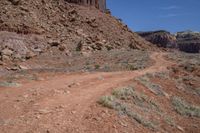 dirt road with rocky terrain at bottom and mountains on either side, blue sky in the background