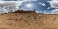 a desert view from a google earth viewing vr viewer lens, with some clouds in the blue sky and a distant orange rock formation in the distance