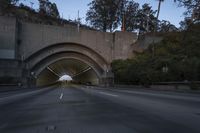 car driving through an old tunnel at dusk along the highway, with lights on, trees and a long wall