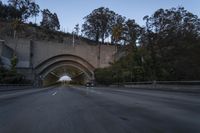 car driving through an old tunnel at dusk along the highway, with lights on, trees and a long wall