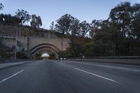 car driving through an old tunnel at dusk along the highway, with lights on, trees and a long wall