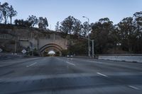 car driving through an old tunnel at dusk along the highway, with lights on, trees and a long wall