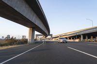 a car driving past a bridge overpass and highway traffic with buildings in the distance
