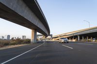 a car driving past a bridge overpass and highway traffic with buildings in the distance