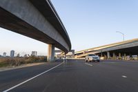 a car driving past a bridge overpass and highway traffic with buildings in the distance