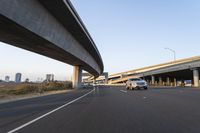 a car driving past a bridge overpass and highway traffic with buildings in the distance