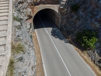 the car is driving through the tunnel near rocks and grass's edge, it is very hard to find where the lines are in the photo