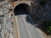 the car is driving through the tunnel near rocks and grass's edge, it is very hard to find where the lines are in the photo