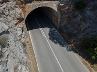 the car is driving through the tunnel near rocks and grass's edge, it is very hard to find where the lines are in the photo