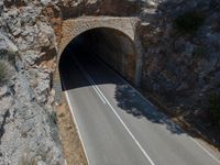 the car is driving through the tunnel near rocks and grass's edge, it is very hard to find where the lines are in the photo