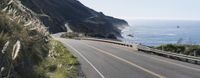 a car driving down a highway that is beside the ocean with a bike on it