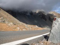 the front end of a car is stopped on a mountainous road as dark clouds loom