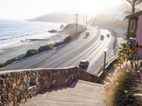 car passing on a beach side road, with light in the background, next to stone stairs