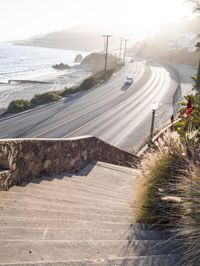 car passing on a beach side road, with light in the background, next to stone stairs