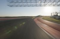 a car on a race track and the sun shining in the background as it passes by