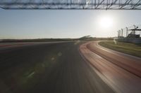 a car on a race track and the sun shining in the background as it passes by