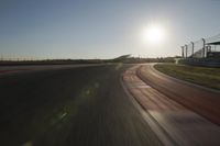 a car on a race track and the sun shining in the background as it passes by