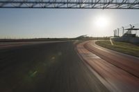 a car on a race track and the sun shining in the background as it passes by