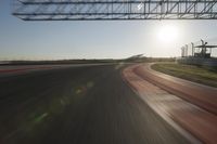a car on a race track and the sun shining in the background as it passes by