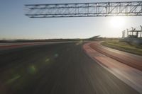 a car on a race track and the sun shining in the background as it passes by