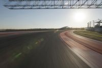 a car on a race track and the sun shining in the background as it passes by