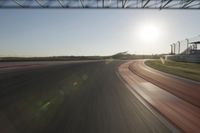 a car on a race track and the sun shining in the background as it passes by
