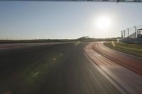 a car on a race track and the sun shining in the background as it passes by