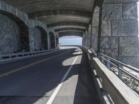 a couple of cars driving under an overpass on a bridge with large windows and a wall