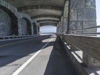 a couple of cars driving under an overpass on a bridge with large windows and a wall